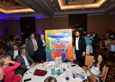 Group of people at a banquet presenting an oversized, colorful product package to the camera.