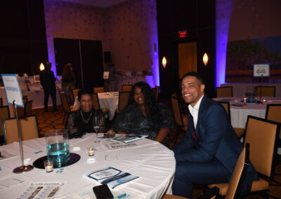 Three people smiling at a table during a gala event with informational materials and dim lighting.