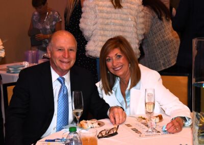 An older man and woman sitting at a banquet table, smiling at the camera, with glasses of champagne.