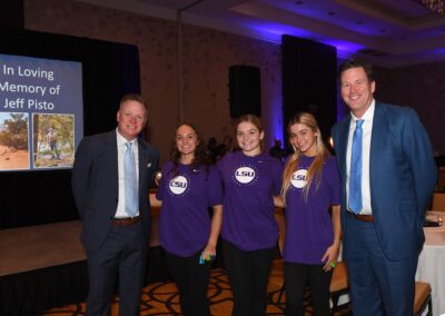 Five people posing in front of a tribute presentation for jeff pisto, three wearing lsu t-shirts.