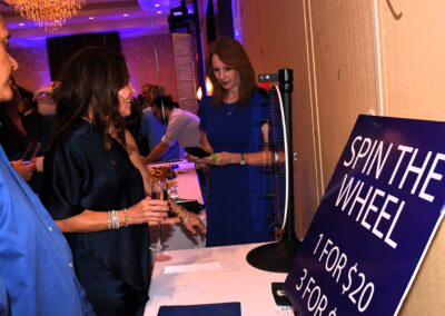 Woman in blue dress engages with a "spin the wheel" game at a lively event, surrounded by other attendees.