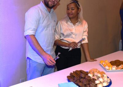 A man and a woman standing beside a table with assorted pastries at a social event.