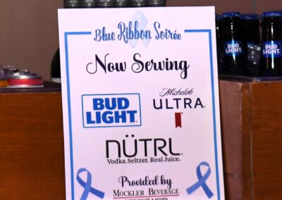 A sign on a bar counter advertising bud light, michelob ultra, and nutrl vodka seltzer, with bottles visible in the background.